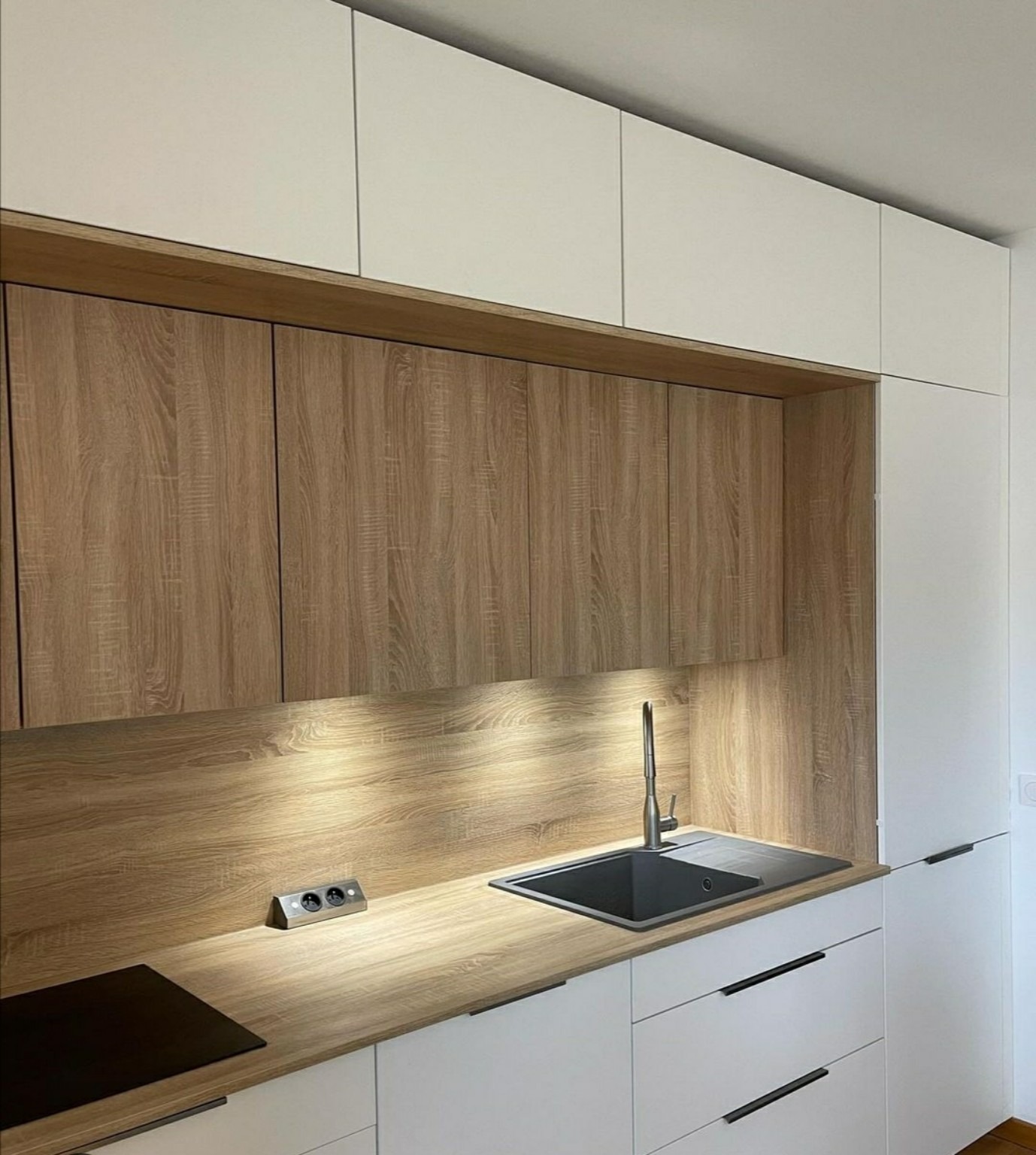 Évier noir, façades blanches et crédence bois dans une cuisine en angle.